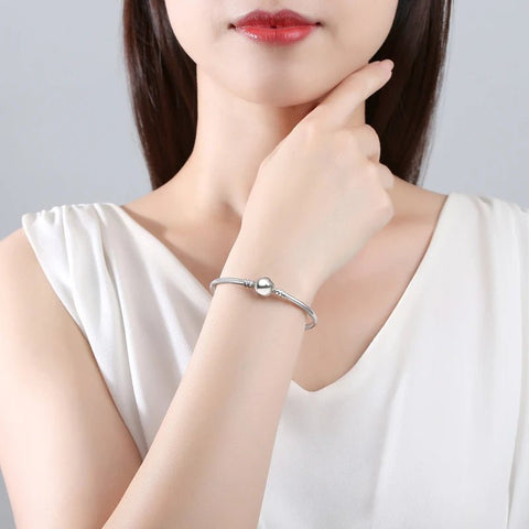 Elegant Sterling Silver Bracelet Pandora Charms Collection - A minimalist silver bracelet with a smooth, round bead worn on a woman's wrist, adding a touch of elegance to her white sleeveless top.