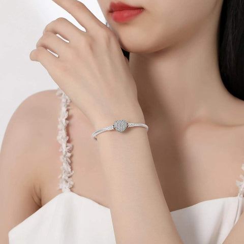 Love Sterling Silver Snake Chain Charm Bracelet Safety Chain - A woman wearing a stylish silver bracelet with a sparkling, round charm embellished with tiny crystals, elegantly complementing her chic white outfit.