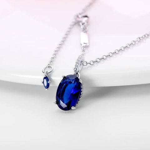 Elegant Blue Sapphire Oval Pendant Necklace in Sterling Silver with Cubic Zirconia Accents - Sterling silver necklace with a blue sapphire oval pendant, laid out on a white background.