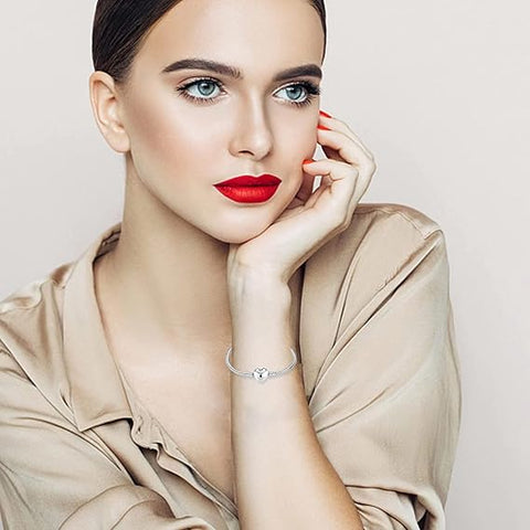 Classic Heart Sterling Silver Snake Chain Charm Bracelet - A stylish woman adorned with a silver bracelet featuring a charming heart detail, complementing her chic beige outfit and bold red lipstick.
