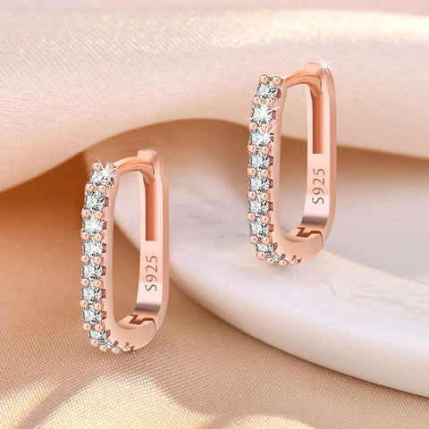 Pair of rose gold hoop earrings with embedded cubic zirconia stones, displayed on a soft fabric background.