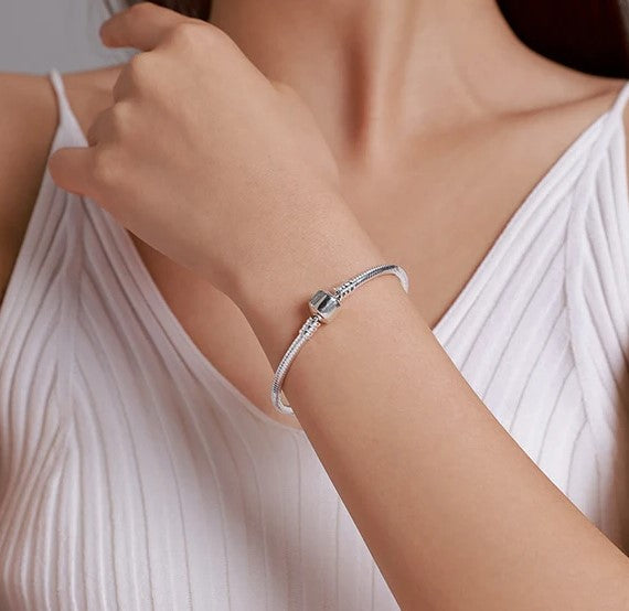 Close-up of a woman's wrist adorned with a sleek silver bracelet featuring a single square charm, highlighting its minimalist and elegant design.