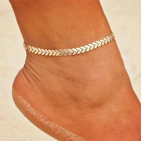 Close-up of an elegant Gold herringbone chain Anklet in Gold, worn on a beach with a sandy background.