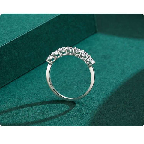 A close-up image of a silver ring with multiple sparkling stones set in a row, displayed on a teal green surface.