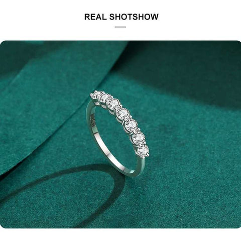 A real-life shot of the silver ring standing upright on a teal green surface, showcasing the row of sparkling stones.