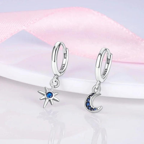 Sterling silver hoop earrings with star and moon charms adorned with blue stones.