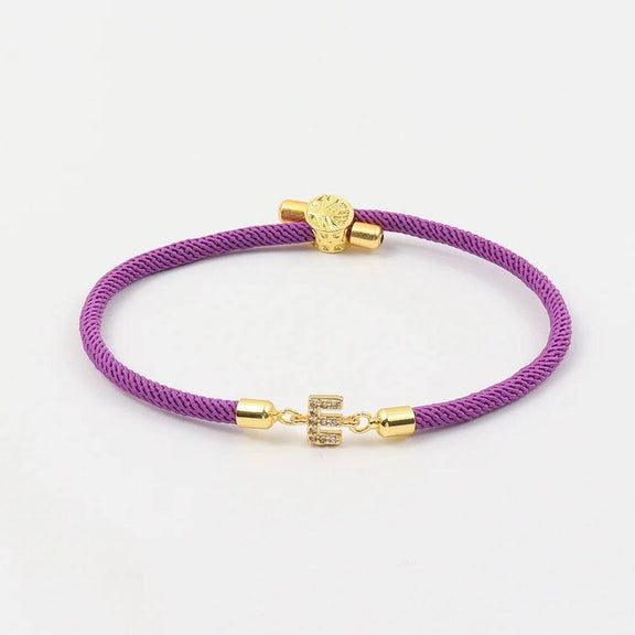 Customizable Initial Bracelet with Crystal Charm in Purple and Green - Purple cord bracelet with crystal initial charm and gold-tone accents.