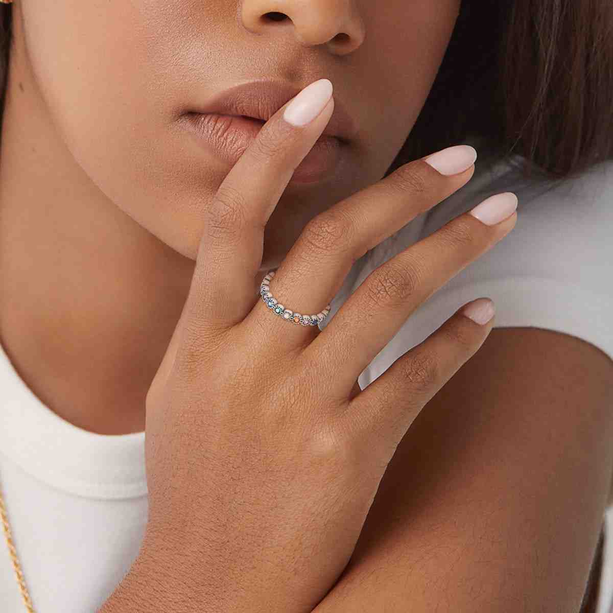 A woman wearing a silver ring adorned with multicolored gemstones, highlighting its delicate and vibrant design on her finger