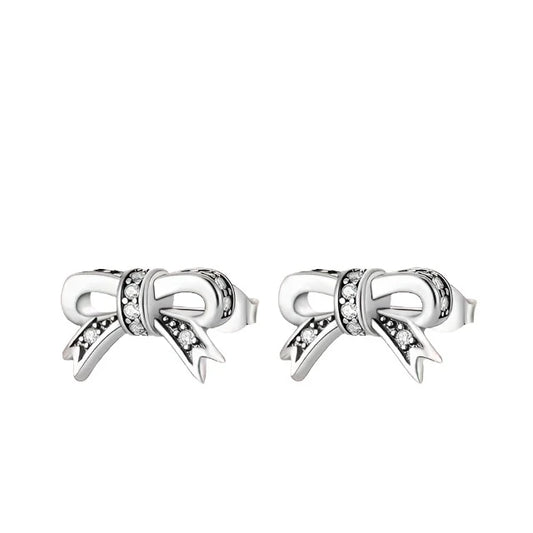 Sterling silver bow knot stud earrings with cubic zirconia accents on a pink background.