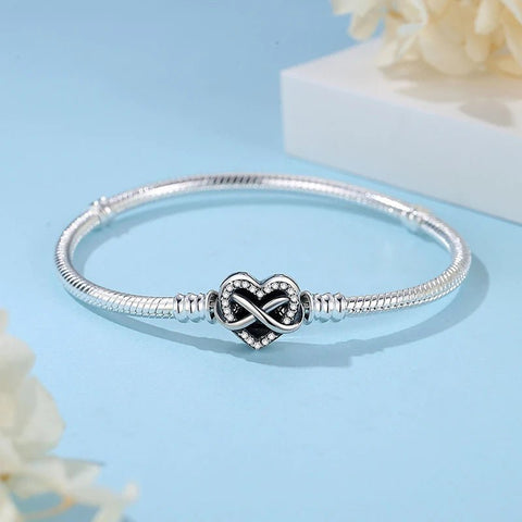 Stylish Affordable Love Bracelet Heart Charm - A delicate silver bracelet featuring a heart-shaped infinity charm adorned with small crystals, elegantly displayed against a light blue background with soft floral accents.
