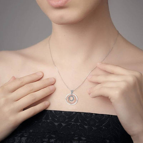 Model wearing an elegant circular pendant necklace featuring three concentric rings in silver, rose gold, and diamond-encrusted silver, showcasing the necklace's fit and style.