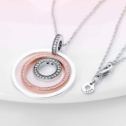 Close-up view of an elegant circular pendant necklace with three concentric rings in silver, rose gold, and diamond-encrusted silver, displayed on a white background.