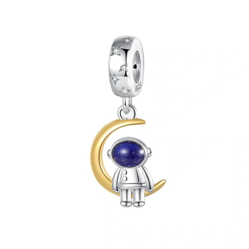 Sterling silver and gold charm featuring an astronaut sitting on a crescent moon with a blue enamel helmet.