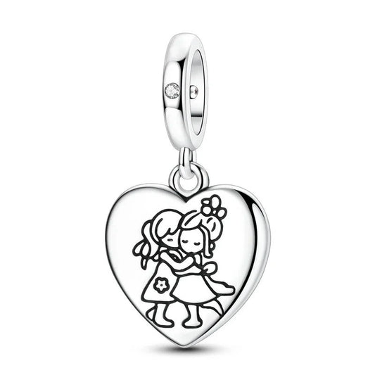 Sterling silver heart-shaped dangle charm engraved with two girls hugging, attached to a polished bail with a small clear crystal, shown on white background