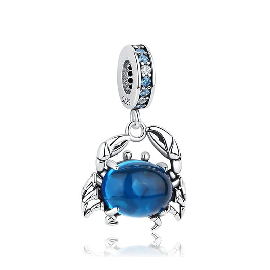 A sterling silver dangle charm shaped like a crab with a deep blue crystal cabochon body, detailed silver claws and legs, and a bale ring set with blue and clear cubic zirconia stones