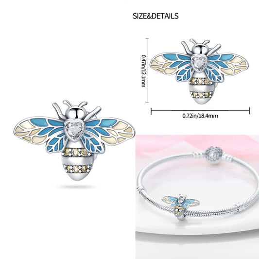 Sterling silver bee charm with blue and cream enamel wings, a heart-shaped crystal,.