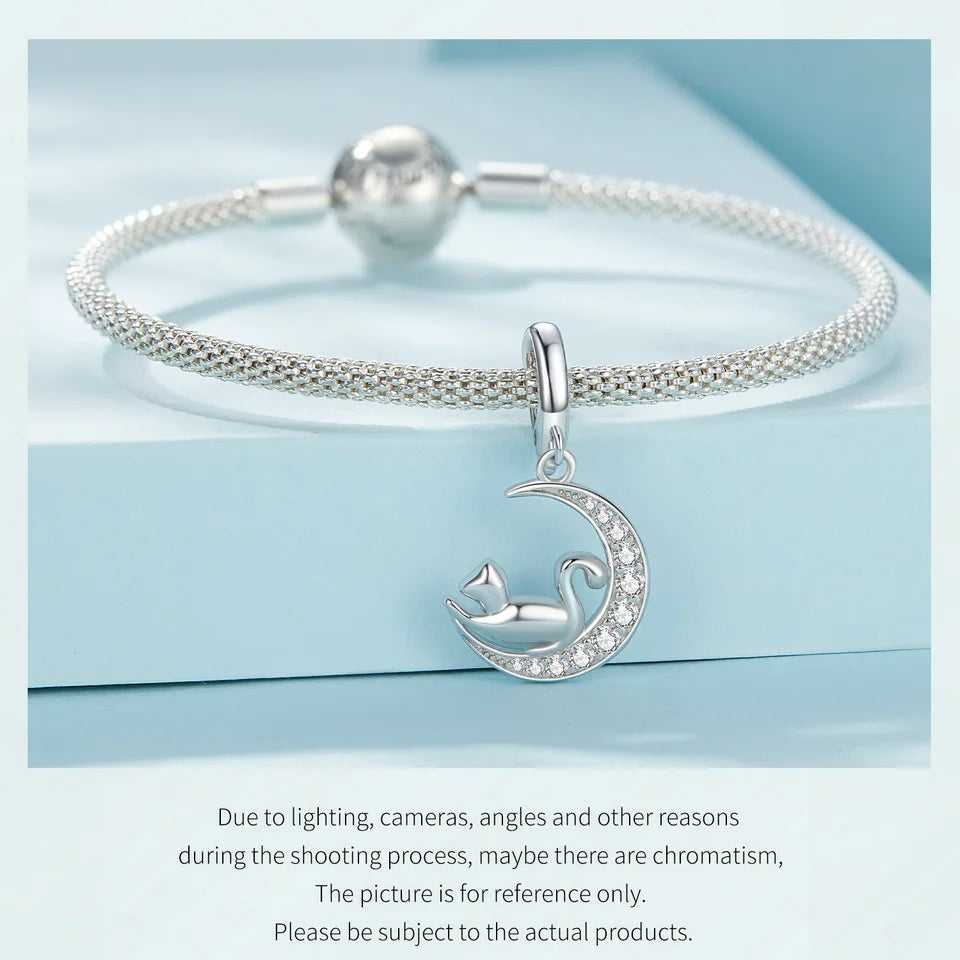 Silver mesh bracelet with a cat on crescent moon charm displayed on a light blue background.