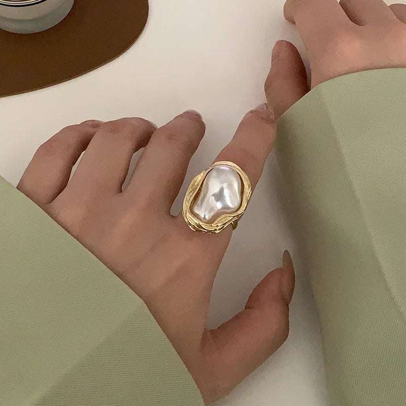 Woman's hand adorned with a gold ring featuring a unique baroque pearl, paired with a chic light green sleeve.