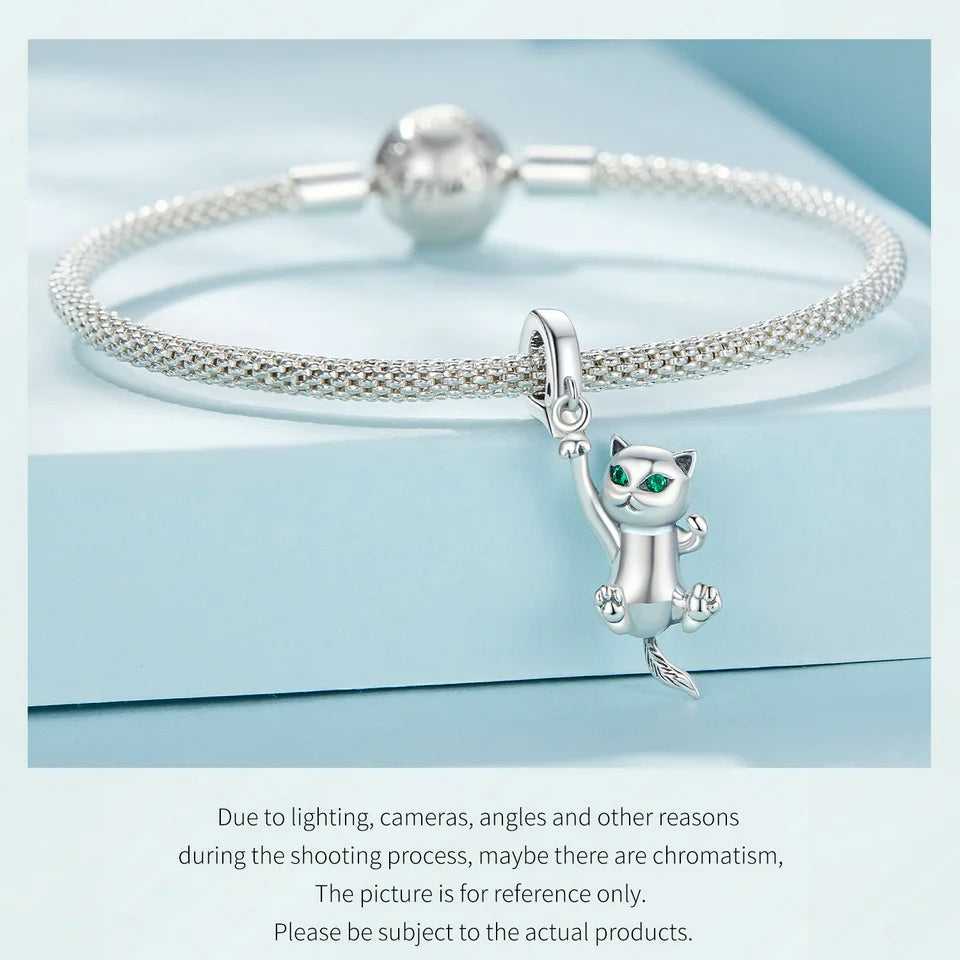 Silver mesh bracelet with a hanging cat charm featuring emerald eyes, displayed on a light blue background.