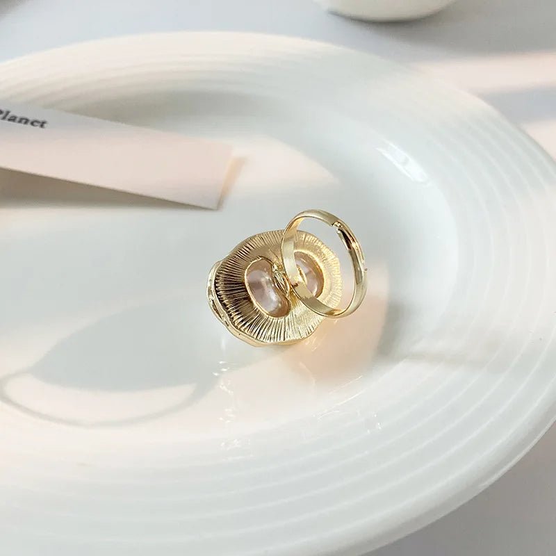 Close-up of a woman's hand holding a gold ring with a baroque pearl centerpiece, emphasizing the ring's luxurious and unique design.