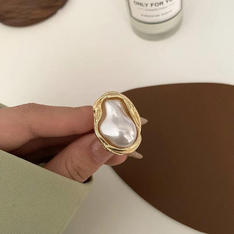 Close-up of a woman's hand holding a gold ring with a baroque pearl centerpiece, emphasizing the ring's luxurious and unique design.