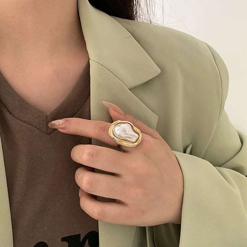 Woman wearing an elegant gold ring with a baroque pearl centerpiece, styled with a chic light green blazer, showcasing the ring's luxurious design.