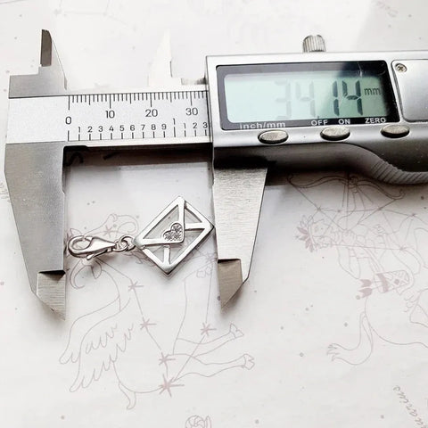 Silver envelope charm being measured.