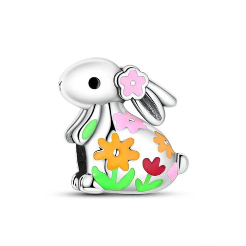 A silver-tone charm depicting a white enamel rabbit sitting upright with colorful enamel flowers in pink, orange, red, and green decorating its body and a pink flower behind its ear