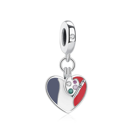 A silver heart-shaped charm with blue, white, and red French flag enamel and a small artist palette detail set with multicolored cubic zirconia stones, hanging from a clip-on bail.