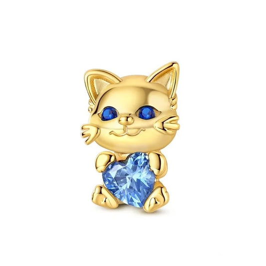 A gold-tone cat charm with blue crystal eyes holding a faceted light-blue heart-shaped crystal, designed as a clip-on charm for charm bracelets