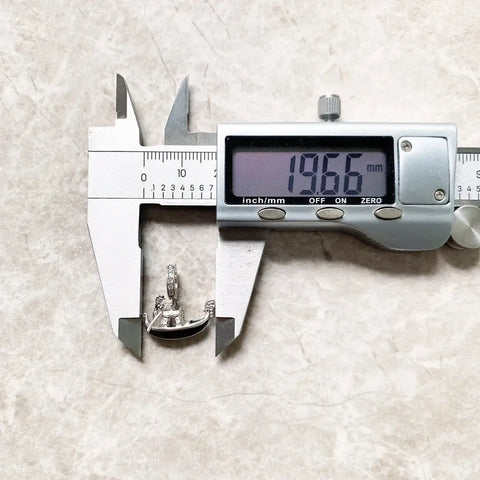 Silver boat pendant being measured.