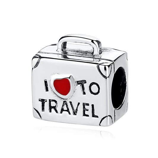 A silver-tone suitcase-shaped charm engraved with 'I love to travel' and a red enamel heart, with a top handle and corner details, shown on a white background