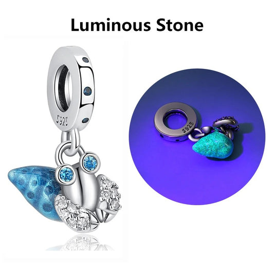 A sterling silver clip-on charm featuring a blue enamel glowing mushroom pendant with cubic zirconia accents, shown in normal light and glowing blue in the dark