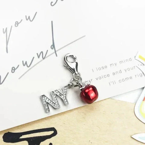 Silver charm with 'NY' and a red apple.