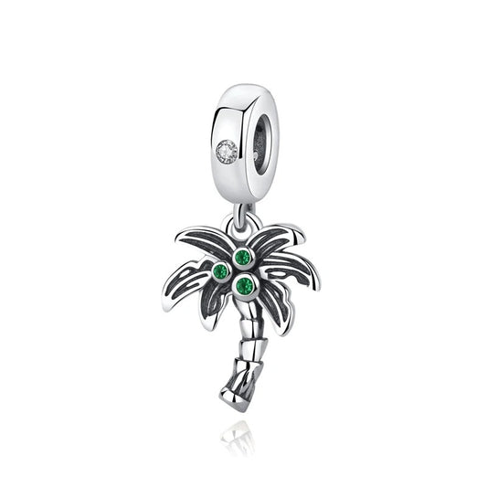 A silver oxidised palm tree dangle charm with three green cubic zirconia crystals in the fronds and a clear crystal on the clip-on bail, photographed on a white background.