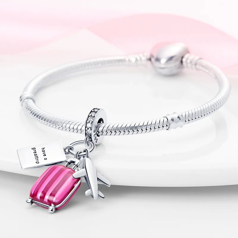 Detailed travel charm with pink suitcase, passport, and airplane in sterling silver.