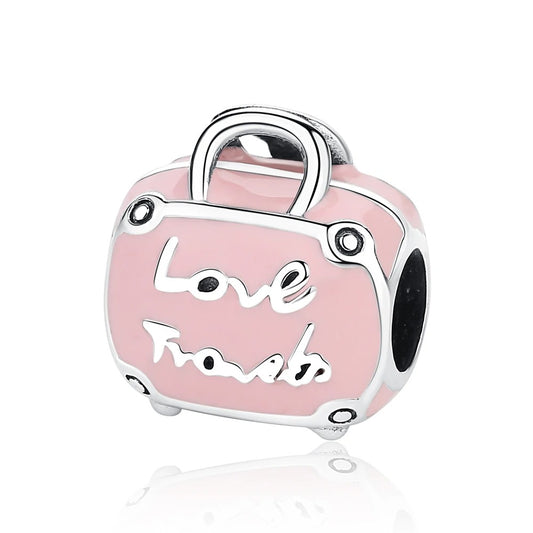A silver-tone and pink enamel suitcase-shaped charm with the words Love Travels in script on the front, featuring a handle and corner details