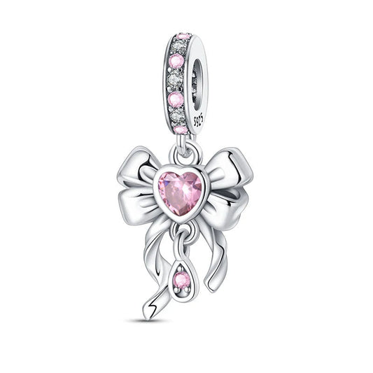 A sterling silver bow charm with a pink heart gemstone at the center, adding a touch of elegance to any jewelry piece.