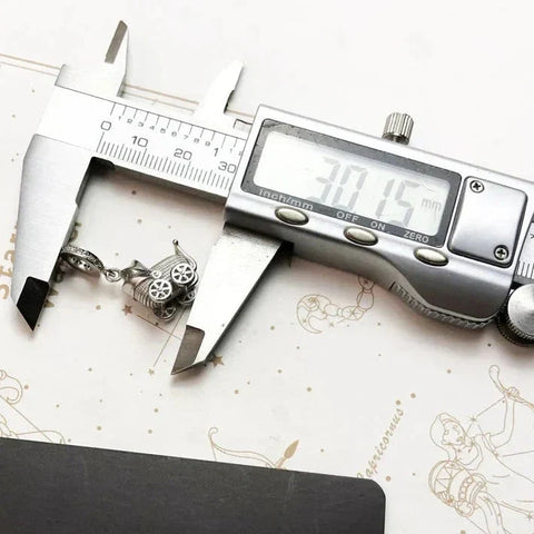 Digital caliper measuring a baby carriage charm.