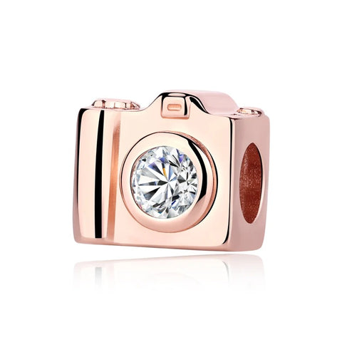 A rose gold camera-shaped charm with a round brilliant-cut clear cubic zirconia stone set as the lens, shown on a white background