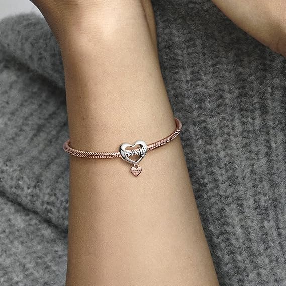 Rose Gold Floral Charm with Pink and White Enamel - Woman wearing a rose gold bracelet with a heart-shaped charm engraved with "Family," featuring a small dangling heart charm, elegantly displayed on a gray knit sweater.