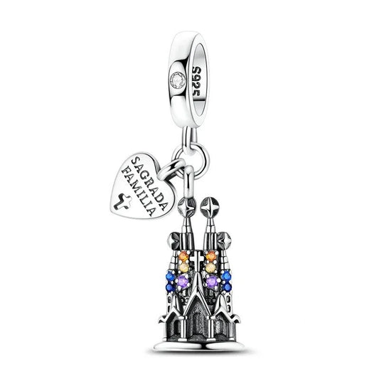 Sterling silver dangle charm depicting the Sagrada Familia cathedral with colorful crystal gemstones and a heart-shaped engraved tag, shown on a white background