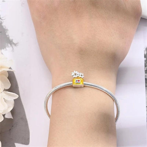 Silver charm bracelet with yellow perfume bottle charm and daisies worn on wrist.