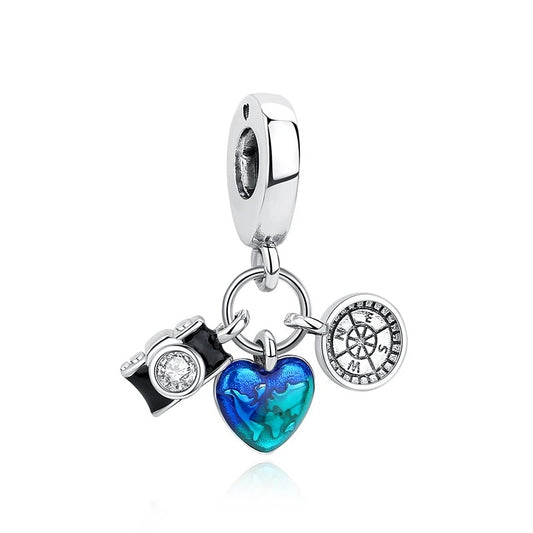 Silver clip-on charm with three dangles: a black enamel camera with crystal lens, a blue Murano-style glass heart, and a silver compass disc with crystal accents