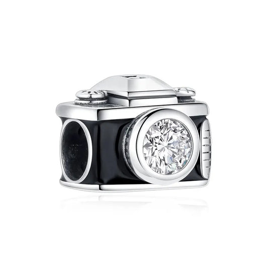 A sterling silver vintage camera charm with black enamel body, a round cubic zirconia crystal lens, and detailed dials on top, photographed on a white background.
