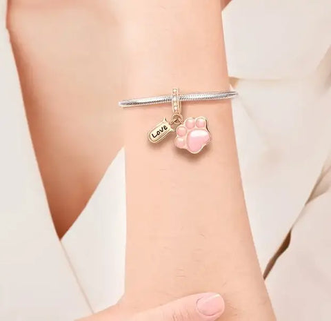 Woman wearing a silver snake chain bracelet with a pink paw print charm and "Love" tag.
