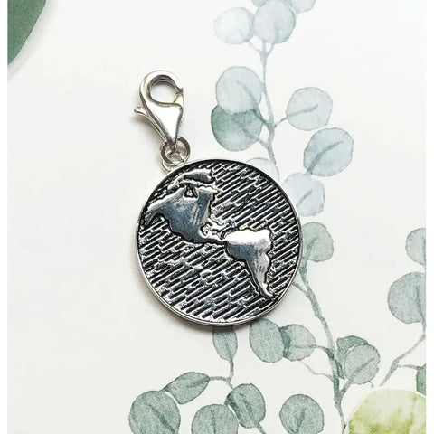 Silver charm with a map of the Americas.